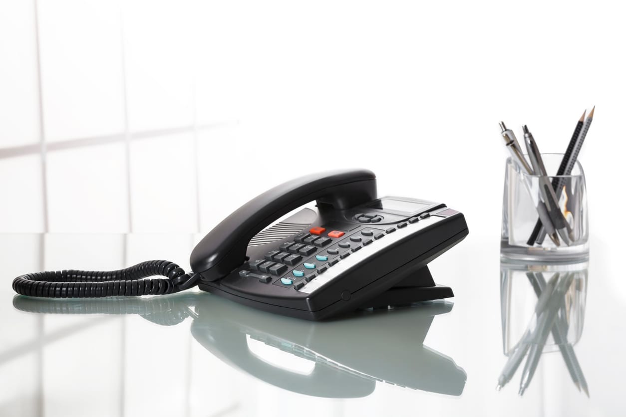 Svart bordtelefon og pennestativ på et lyst skrivebord